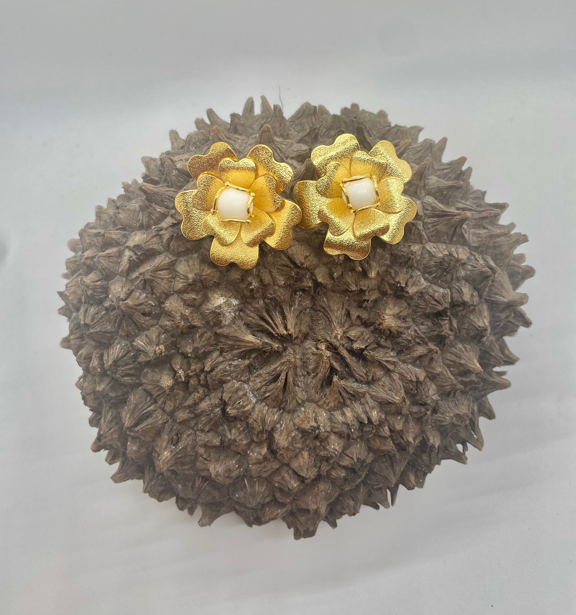 A pair of earrings featuring a golden flower design with tagua beads