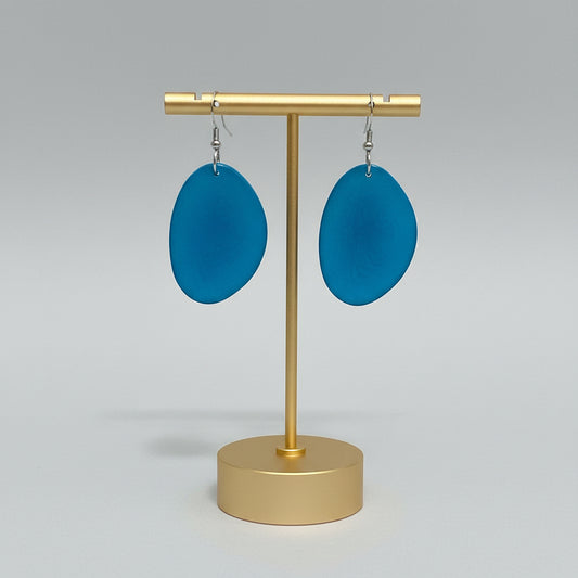 A pair of turquoise earrings made from sliced tagua nuts, displayed on a beige background.